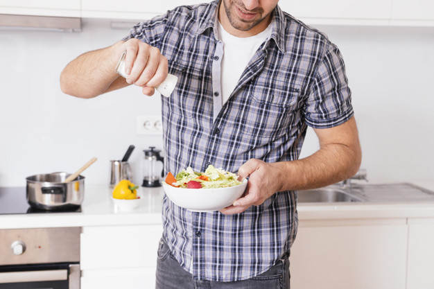 primer-plano-hombre-joven-que-agrega-sal-ensalada-verduras-mientras-cocina-cocina_23-2148120516.jpg